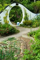 Moon gate marks passage from the kitchen garden to the Wandering Garden, framed by trained fruit trees, Rudbeckias and Tagetes - Marigolds with Onions ready to harvest in the foreground. Beggars Knoll, Newtown, Westbury, Wiltshire, UK
