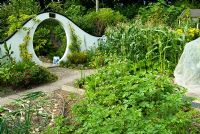 Moon gate marks passage from the kitchen garden to the Wandering Garden, framed by trained fruit trees, Rudbeckias and Tagetes - Marigolds with Onions ready to harvest in the foreground. Beggars Knoll, Newtown, Westbury, Wiltshire, UK

