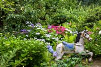 Wood horse backed by Hydrangea macrophylla and Malus - Apple tree