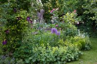Romantic garden with mixed border of Rosa 'Louise Odier', Alchemilla mollis, Buxus, Clematis 'Warzawska Nike' and willow ornaments. 