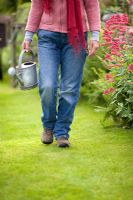 Woman wearing jeans and gardening boots carrying a vintage galvanised watering can