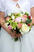 Girl in a white dress holding a bridesmaid bouquet of roses and peony