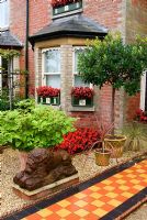 Front garden of Victorian terraced house features a tiled path beside gravelled area containing statuary and planting including Begonia 'Big Boy' and Cordylines. The Secret Garden at Serles House, Wimborne, Dorset, UK
