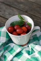 Plums in pottery mug with check cloth