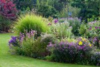 Perennial border with ornamental grass, glass objects and Aster amellus 'Veilchenkönigin', Aster novi-belgii 'Royal Velvet', Clematis, Miscanthus sinensis 'Gracillimus' and Physostegia virginiana 'Vivid'