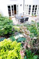 Elevated view of sloping small modern garden with white painted walls, terrace and tiered planting. 
