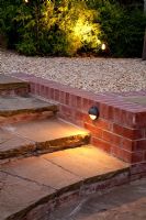 Brick edged stone steps and gravel patio lit up at night. Fargesia nitida - Bamboo