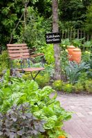 Potager with brick paths, wooden chair and beds with Brassica oleracea nero di toscana - Cavolo Nero, Beta vulgaris 'Bright Lights', Rhubarb forcer and Tagetes - Marigolds
