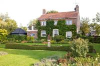Country house with Hydrangea petiolaris. Lawn, Buxus hedges and borders - Lipkje Schat Garden