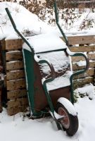 Wheelbarrow covered in snow next to compost heap in winter