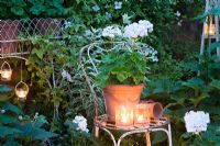 Glass jar tealights lighting Geraniums in containers in white garden