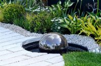 Water feature with reflecting ball, surrounded by gravel and white bricks.  