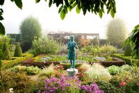 The Formal Garden, with knot garden made of Buxus - Box and Berberis, contains a statue of a girl holding the lamp of wisdom by Nathan David. It is surrounded by tall Taxus - Yew hedges and featues a vine covered pergola - Waterperry Gardens, Wheatley, Oxfordshire, UK