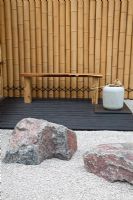 A seating area with rocks and gravel path backed by a bamboo fence in the  Japanese themed garden - 'Less and More' garden - RHS Hampton Court Flower Show 2011 