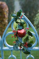 Blue metal gate decorated with bauble and Ilex 'J C Van Tol' - Holly sprig
