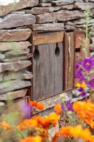 Insect hotel or shelter with Geum 'Prinses Juliana' and Verbascum phoeniceum 'Violetta' in a dry stone wall - The RBC New Wild Garden at RHS Chelsea Flower Show 2011