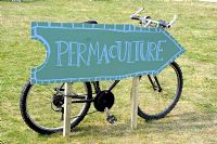 Permaculture direction sign with bicycle behind, Camden Green Fair, London UK
