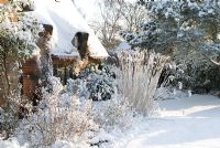 Thatched and brick cottage in the snow, border includes Spiraea and the grass Miscanthus sinensis 'Silberfeder.'  Gowan Cottage