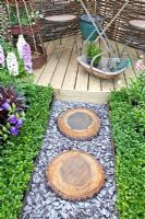 Corner of small garden with path of slate chippings and stepping stones made from sawn logs