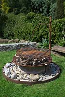 Rusty firepit sitting on a large stone boulder, with fir cones and kindling

