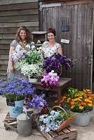 Rachel and Jo with display of flowers outside the packing shed, in buckets, baskets and galvanised tubs on apple crates. Calendula officinalis - Pot marigold, Salpiglossis 'Kew Blue', Campanula lactiflora 'Anna Loddon', Cornflower 'Blue Ball', Sweet Peas, DIll, Ammi majus - Green and Gorgeous 
