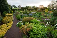 The Flower Garden features strong blocks of box and yew that frame cottage garden plants and flowers, including Euphorbia, Polemoniums and Geraniums - Herterton House, Hartington, Northumberland, UK