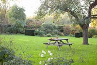 Wooden picnic bench in autumn garden with  Malus domestica 'Notaris'. Tuin de Villa, Netherlands 
