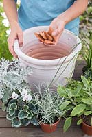 Step by step for planting silver and grey themed container - adding broken pieces of pot to aid drainage