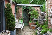 Granite patio with bench, chair, decorative stone angel and plants in containers - Parthenocissus, Rhododendron and Thuja
