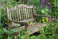 Wooden bench surrounded by a tightly planted border including Rosa, Allium 'Purple Sensation' seedheads, Nepeta, Stipa gigantea, Helinathus and Geranium - The Lizard, Wymondham, Norfolk