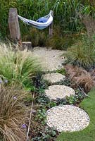 Hammock in small gravel area surrounded by ornamental grasses and path of circular containers filled with gravel, bark chippings and Viola in the 'One Man Went To Mow' garden  RHS Tatton Flower Show 2012