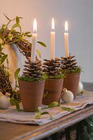 Candles with terracotta holders decorated with fir cones and moss