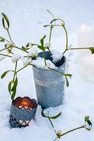 Snowy mistletoe sprigs in silver pot with tealight