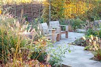 Wooden chairs in Autumn garden with planting of Pennisetum and Fagus sylvatica
