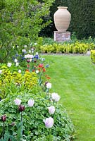 Long spring bed with Tulipa, Euphorbia, Anemone and Geranium leading to large urn feature backed by Taxus hedge - Abbeywood gardens, Cheshire