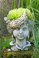 A stone head of an elf planted with Sedum 