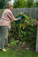 Woman placing tops of potato plants on to compost heap