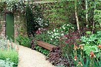 Gravel path with lush border planting, Clematis on brick wall and garden bench - The Largest Room in the House, RHS Chelsea Flower Show 2008 