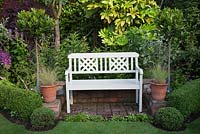 Painted bench on brick terrace with Buxus balls and low Buxus hedge, standard Bay trees and potted grasses - Garden Neighbours 
