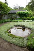 Circular pond surrounded by planting of Lavender, Anaphalis, Antennaria dioica, Apple and Plum trees, Buxus and Taxus topiary balls and hedges, Artemisia 'Silver queen', Brunnera, Lavender, Veronica spicata with brick and terracotta tile surfaces - Ulla Molin 
