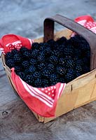 A wooden punnet of fresh blackberries on a rustic wooden surface
