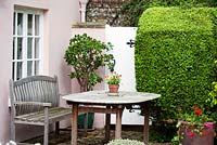 Wooden bench and table in front of Manor House with clipped hedge and containers - Ocklynge Manor