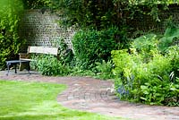 Decorative, winding brick pathway alongside lawn with old wooden bench - Ocklynge Manor