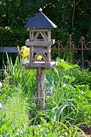 Wooden bird feeding house in a kitchen garden, antique iron garden fence in background 