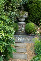 Secluded garden path leading to brick and flint panel with stone feature on plinth