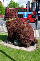 Floral sculpture of Dick Whittington's cat, made from a wire frame covered with sempervivum, sits watching a passing bus on the Holloway Road, London Borough of Islington, UK