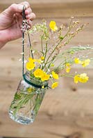 Wild buttercups and grasses arranged in glass jar vase
