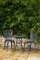 Shady corner of garden with bistro table and chairs. Planting in raised bed of Phyllostachys aureosulcata f. spectabilis
