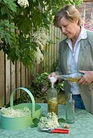 Woman making Elderflower Vinegar - adding cider vinegar to blossoms in a bottle