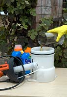 Pouring correct amount of weedkiller into garden sprayer prior to adding water, wearing protective rubber gloves for safety